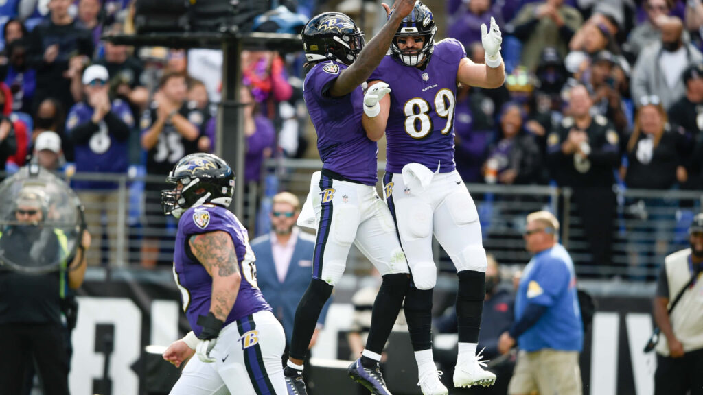 Mark Andrews mid-air celebrating big play with Baltimore Ravens teammates on vibrant field background Wallpaper