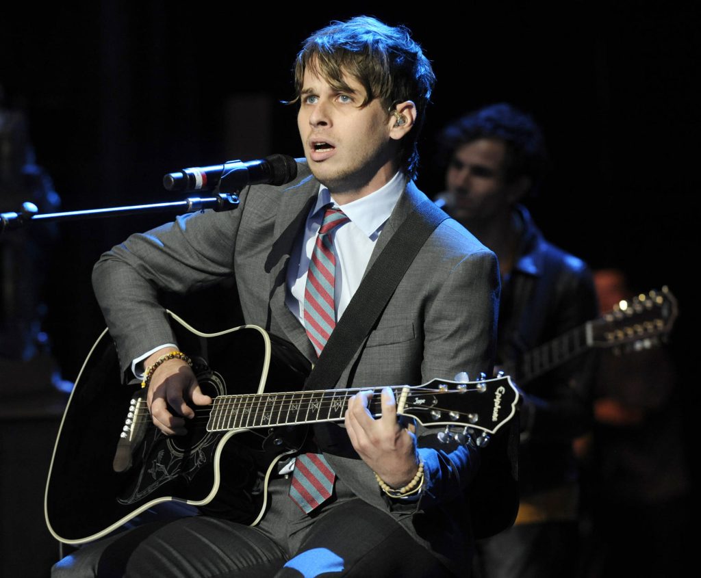 Mark Foster of Foster the People plays acoustic guitar in suit during moody live concert performance Wallpaper