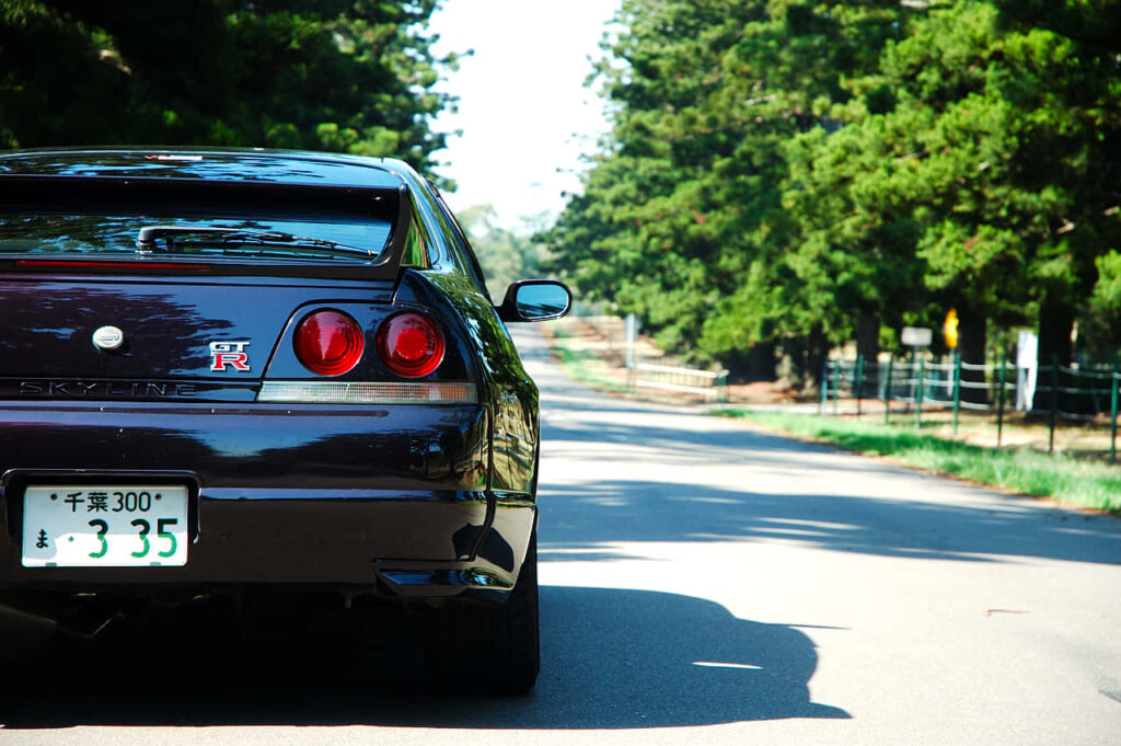 Maroon Nissan Skyline R33 GTR driving on a tree-lined road showcasing classic Japanese performance Wallpaper