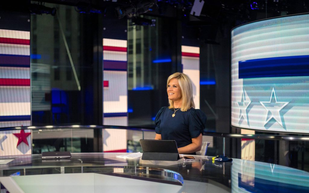 Fox News host Martha MacCallum smiling at desk in studio patriotic backdrop red white blue tones Wallpaper
