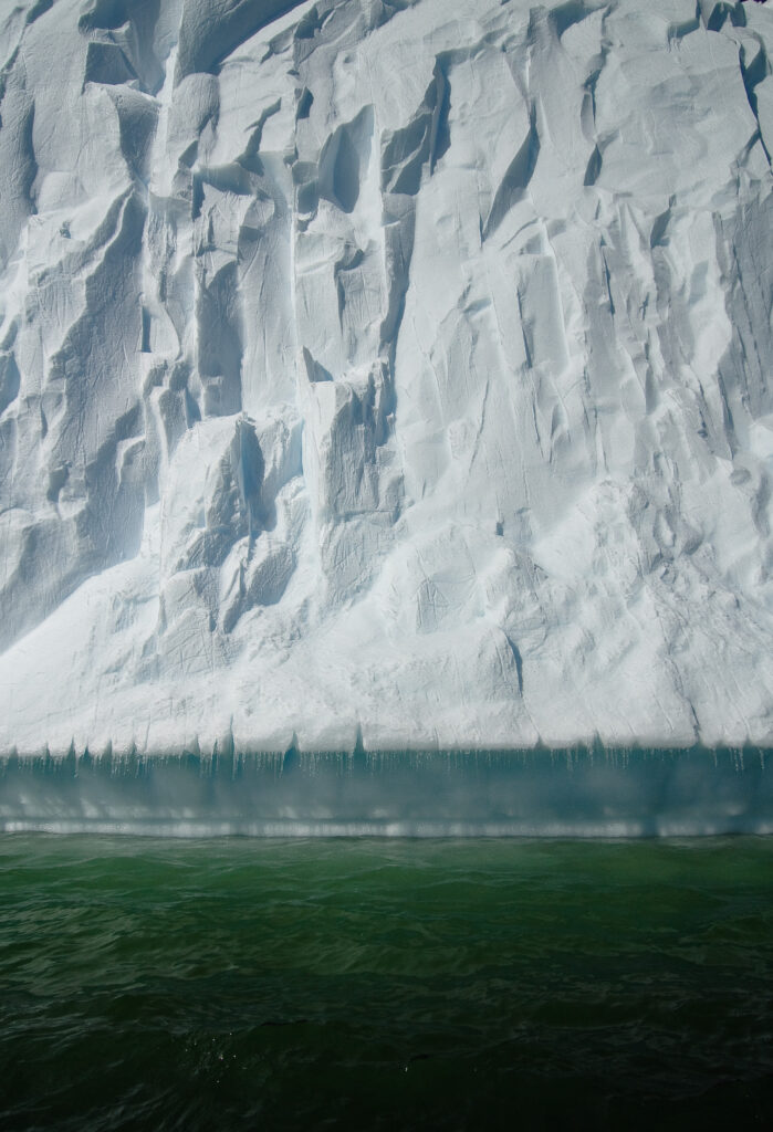 Massive iceberg with intricate snow and rugged ice textures in icy green Antarctic waters wallpaper