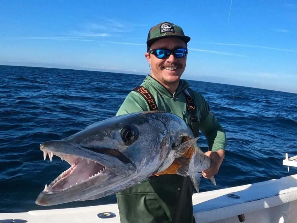 Fisherman proudly holding large barracuda on boat with deep blue ocean and clear sky background Wallpaper