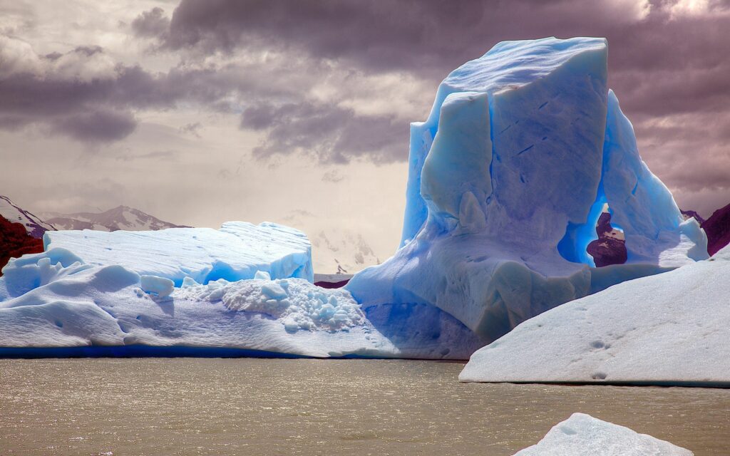 Massive blue ice formations rise from arctic ocean under dramatic cloudy skies wallpaper background