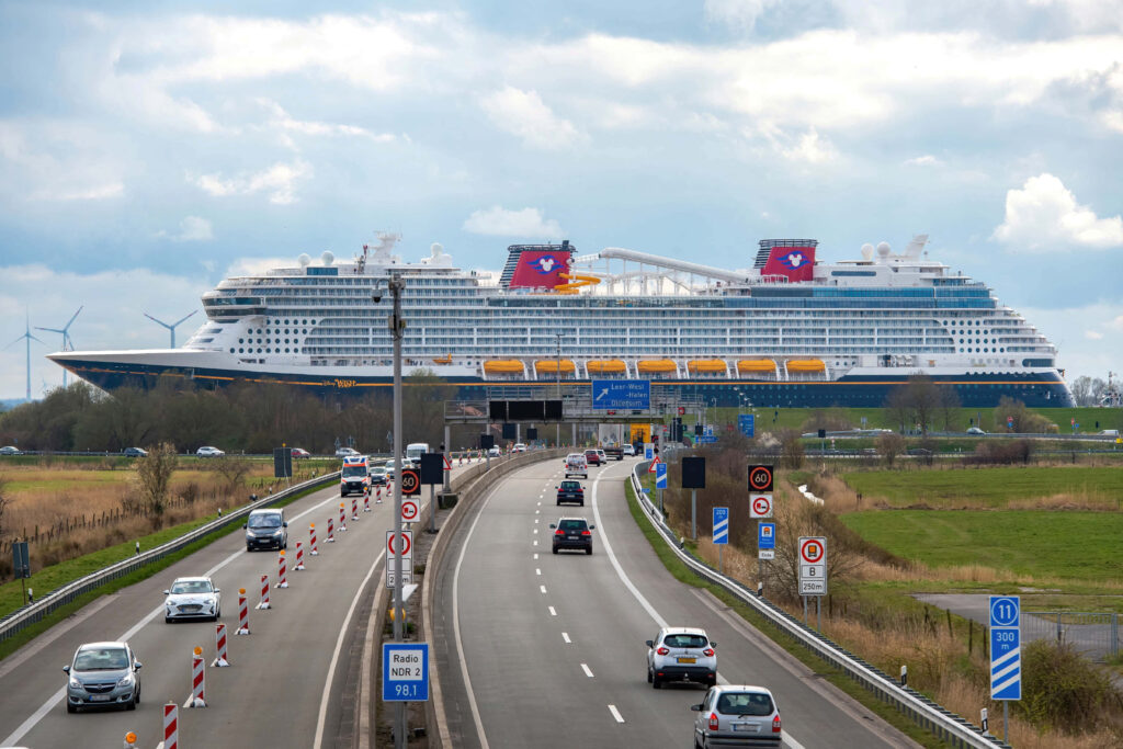 Massive cruise ship crossing urban road with cars traffic signs bright colors cloudy sky wallpaper