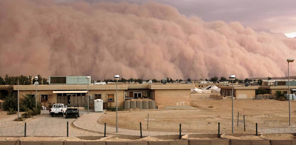Massive dust storm engulfing low-rise buildings under dramatic sky in swirling sand wall wallpaper