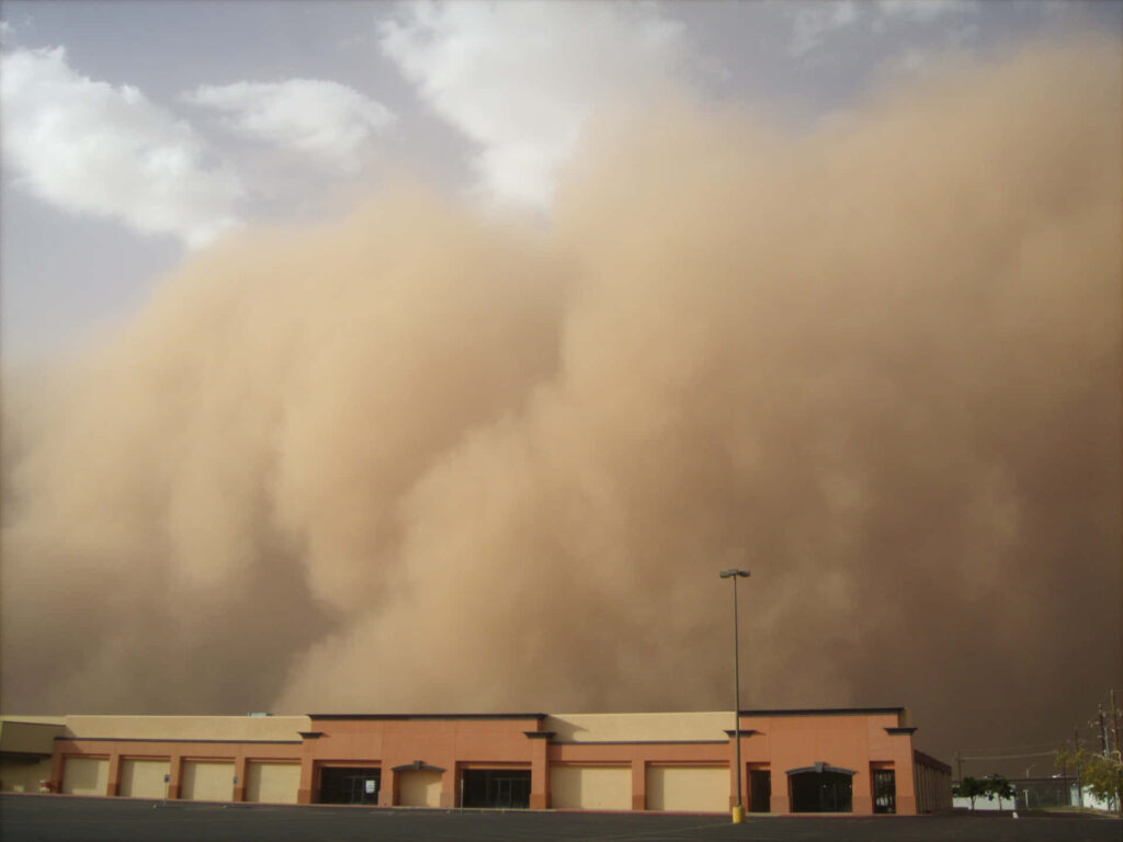Massive dust storm engulfs low building under hazy sky with warm muted sunlight background Wallpaper