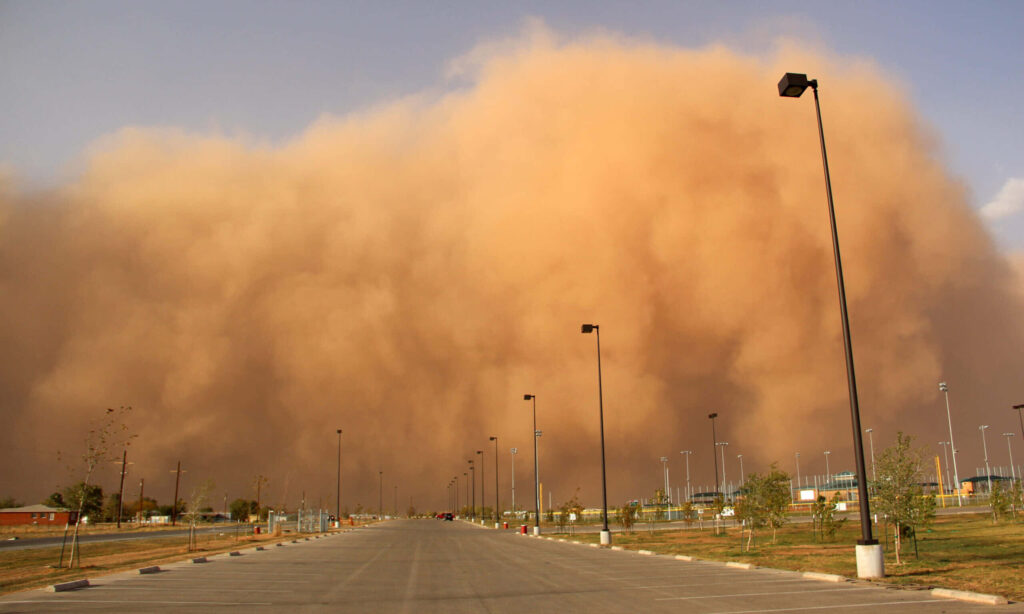 Massive dust storm with orange haze approaches empty city road lined with streetlights dramatic clouds Wallpaper