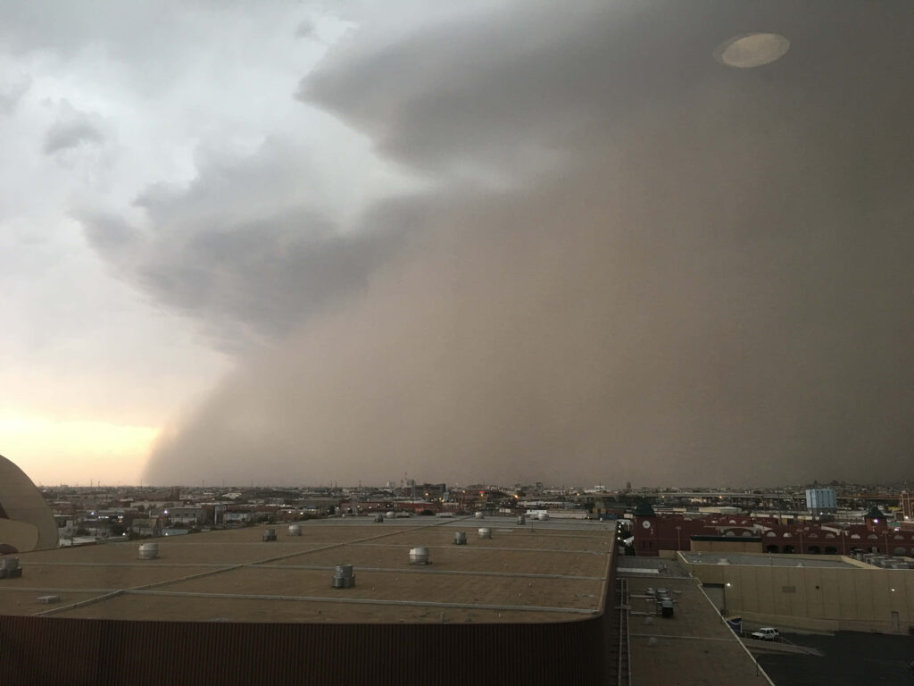 Massive dust storm approaches city skyline under dramatic overcast sky tones wallpaper background