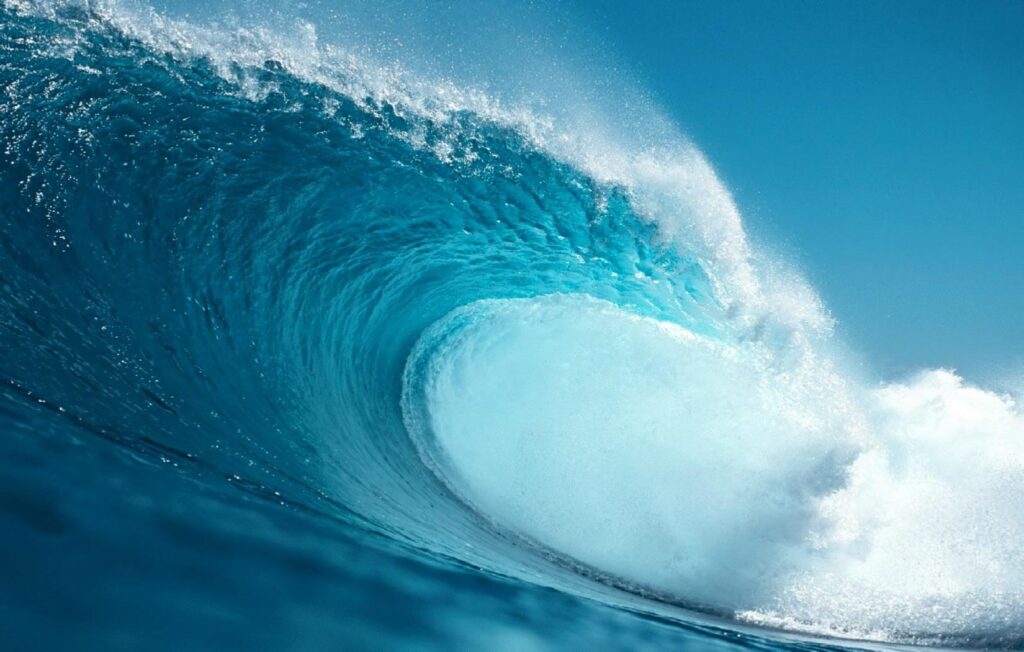 Massive ocean wave wallpaper showing transparent blue water energetic splashes and dynamic movement