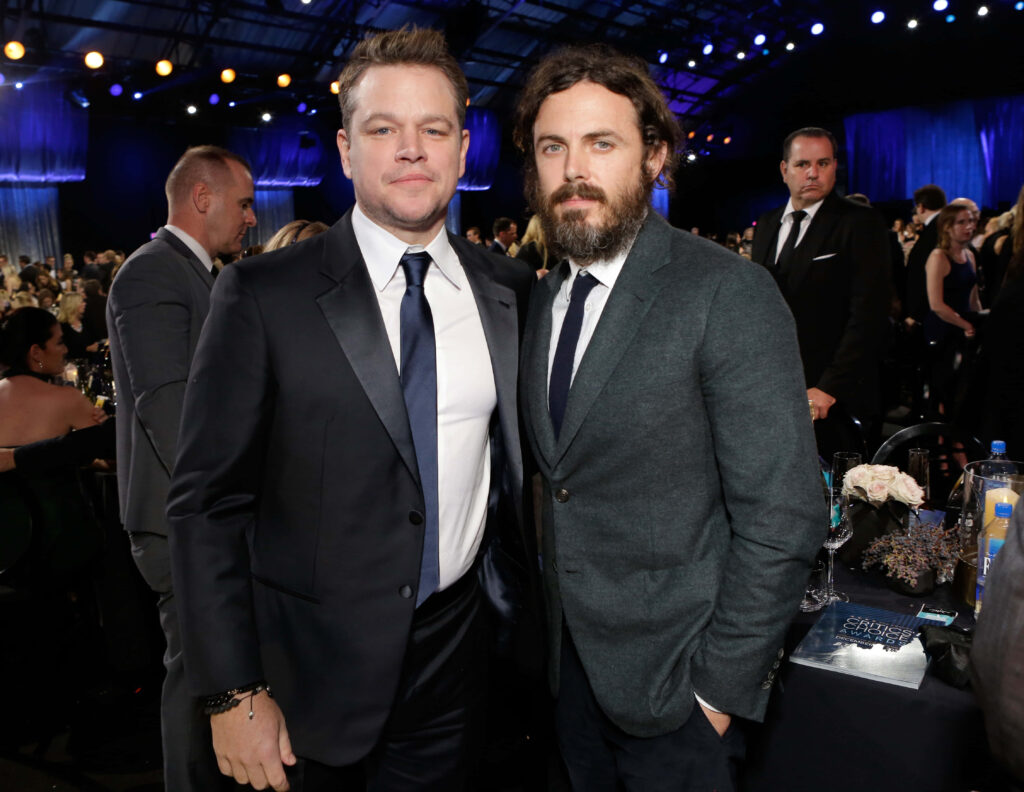 Matt Damon and Casey Affleck in sharp suits at elegant Hollywood event with ambient lighting Wallpaper