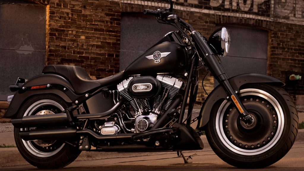 Matte black Harley-Davidson Fat Boy with solid disc rims and chrome engine at sunset brick wall Wallpaper