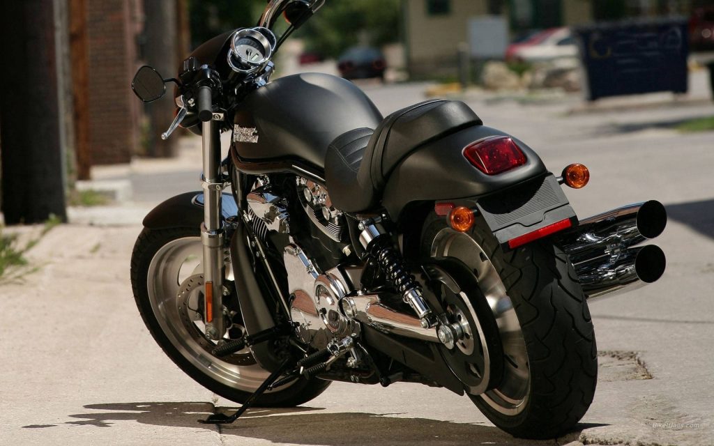 Matte black Harley-Davidson V-Rod rear 34 view with chrome exhaust on urban street background Wallpaper