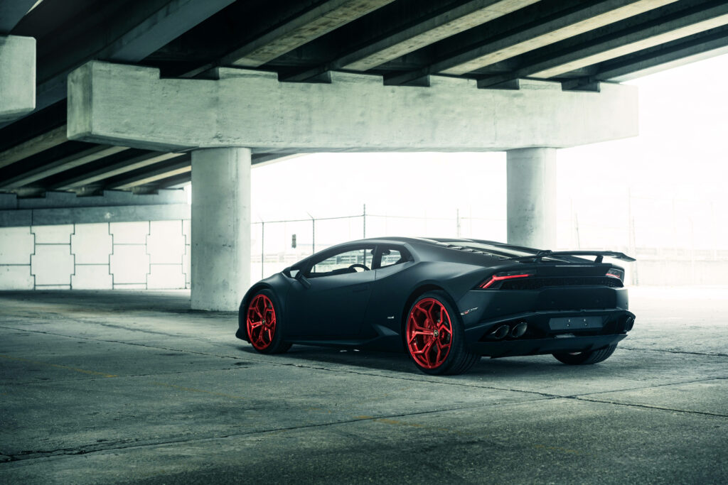 Matte black Lamborghini Huracan with red rims parked under industrial bridge 4k wallpaper