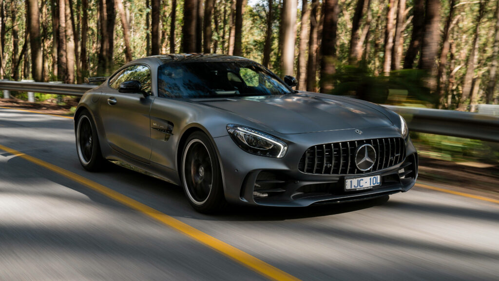Matte black Mercedes AMG GT R driving on sunlit forest road showcasing power and style wallpaper