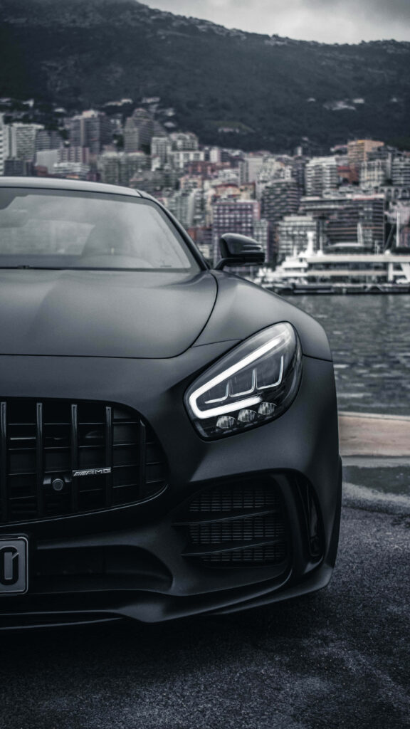 Matte black Mercedes AMG GT R sports car by waterfront cityscape luxury urban wallpaper background