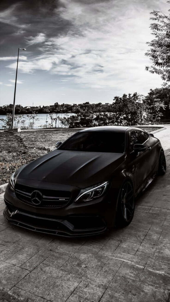 Matte black Mercedes parked on riverside road with sleek design and moody sky background Wallpaper