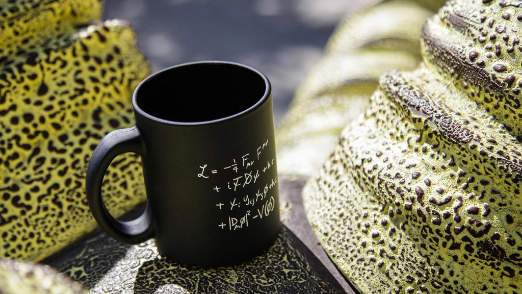 Matte black mug with Standard Model Lagrangian equation on yellow green abstract sculptural background Wallpaper