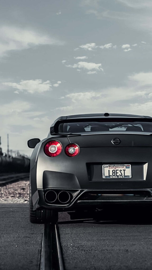 Matte black Nissan GTR R35 rear view with bold taillights under dramatic sky wallpaper background