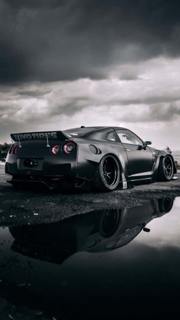 Matte black Nissan R35 GTR parked on wet asphalt with reflection and dramatic cloudy sky background Wallpaper