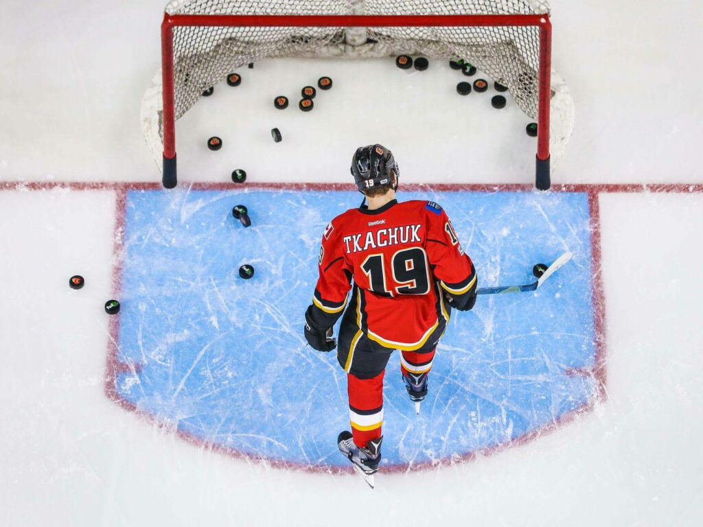 Matthew Tkachuk Calgary Flames warms up in red jersey number 19 near goal with pucks on ice Wallpaper