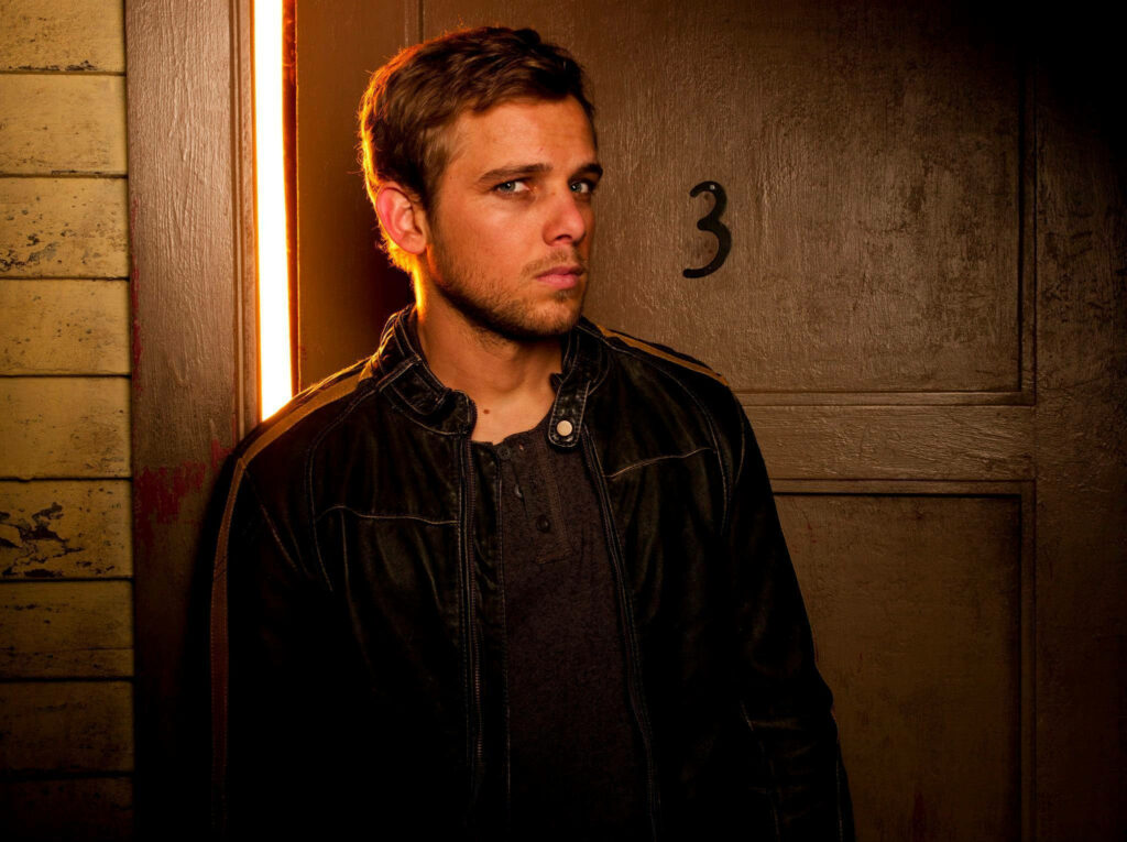 Max Thieriot as Dylan in Bates Motel wearing dark leather jacket by dimly lit door background Wallpaper