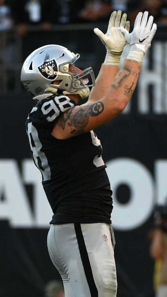 Maxx Crosby in Raiders uniform celebrates with raised arms during game vs Cincinnati Bengals crowd Wallpaper
