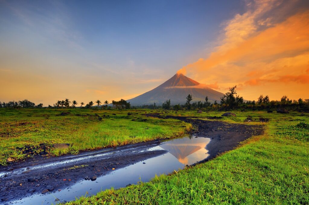 Mayon Volcano at sunset over green park with mountains and water reflection beautiful landscape Wallpaper