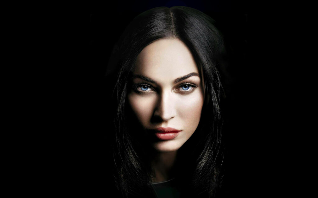 Megan Fox portrait emerging from black shadows showcasing captivating gaze and sharp features Wallpaper