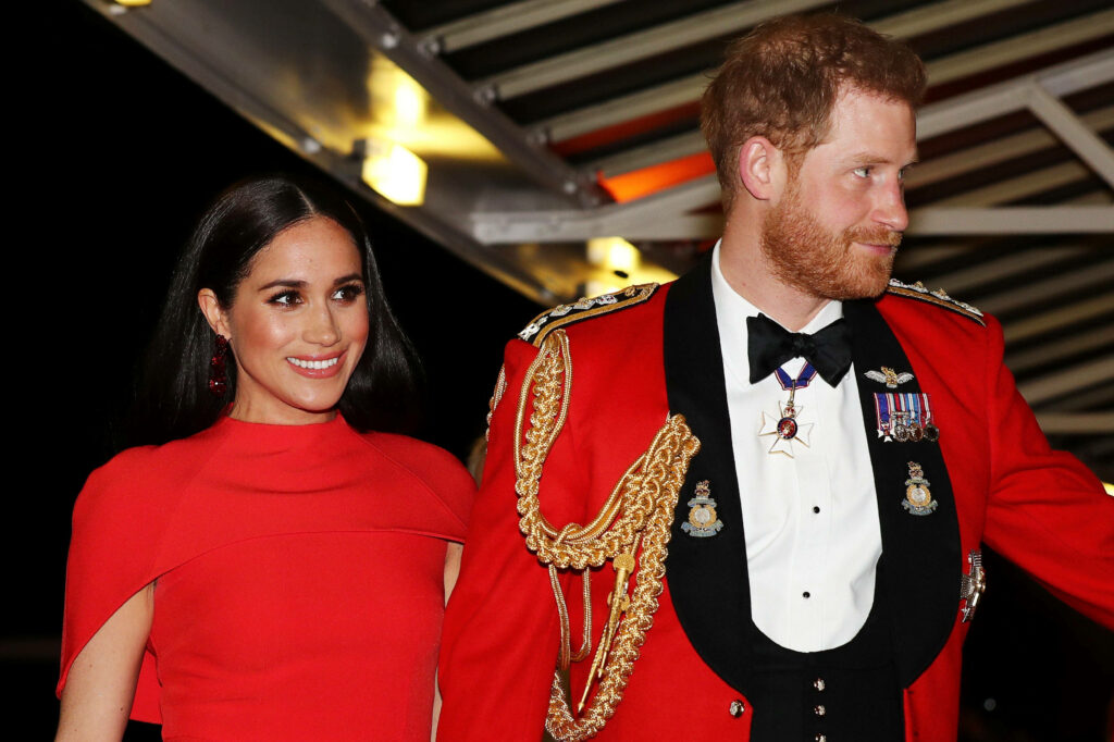 Meghan Markle and Prince Harry in elegant matching red outfits against stylish backdrop wallpaper