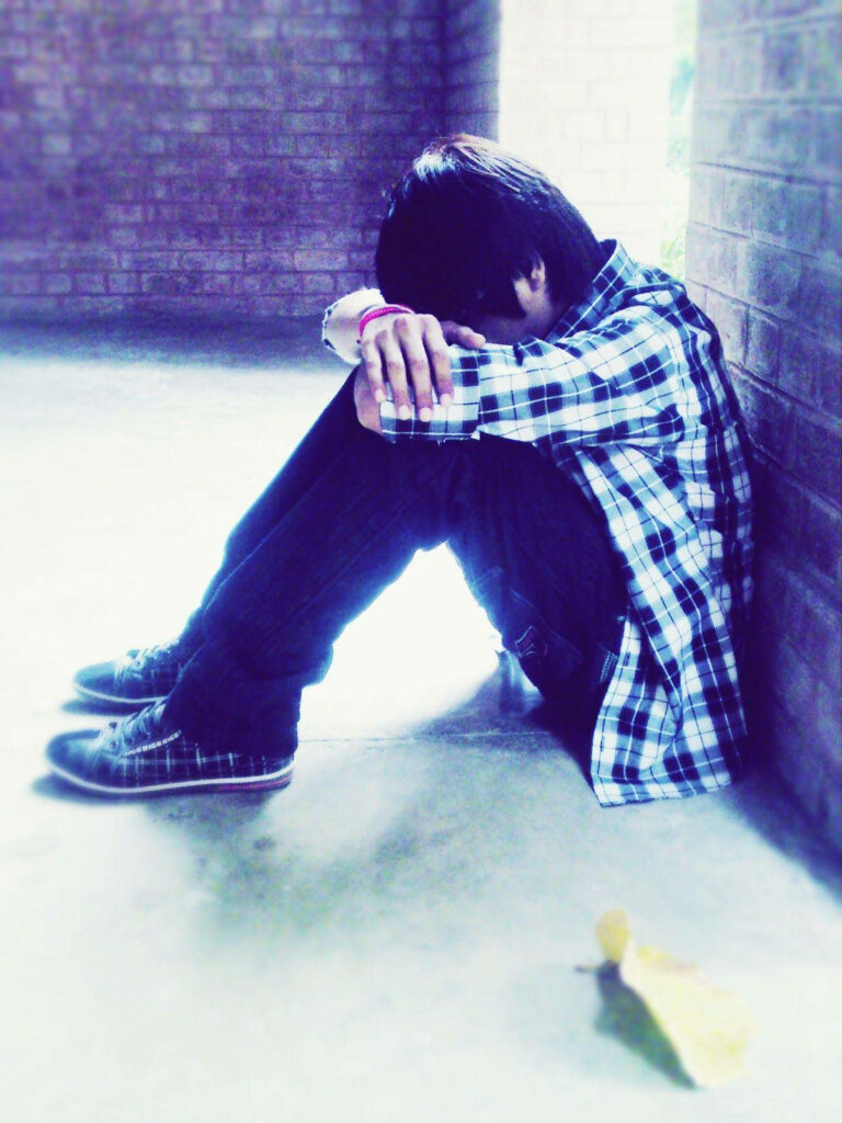 Solitary emo figure in checkered shirt against brick wall with blue tones and soft light background Wallpaper