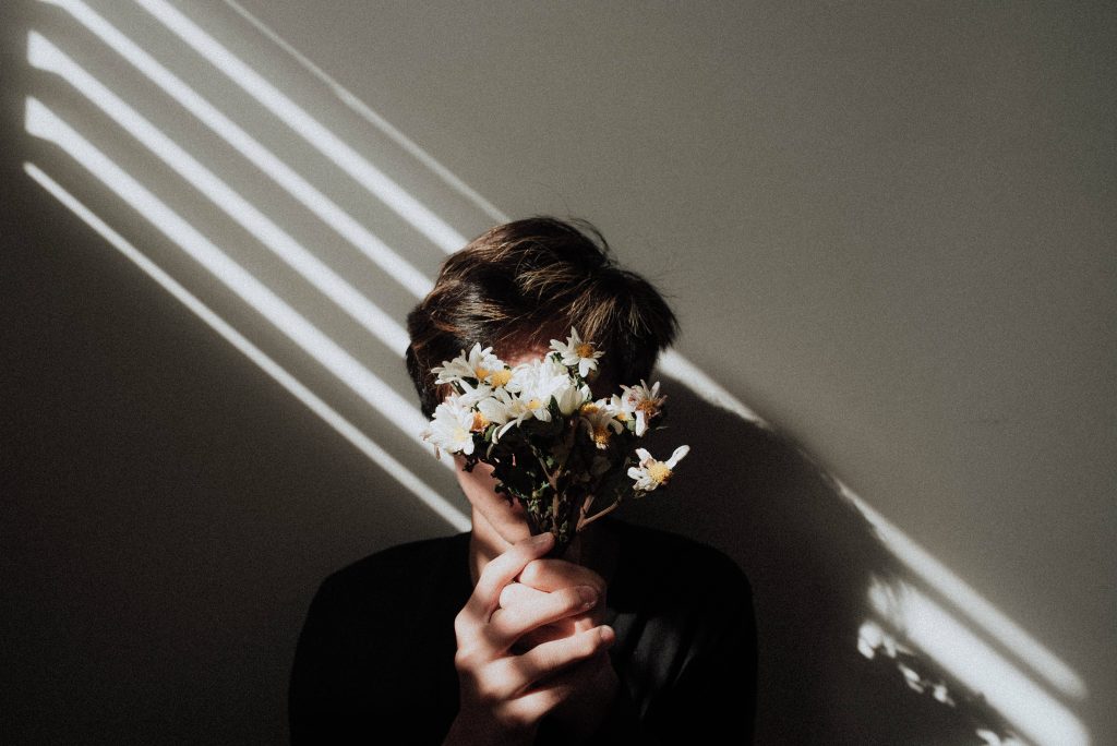 Sad aesthetic wallpaper of person hiding face with white flowers in striped sunlight shadows