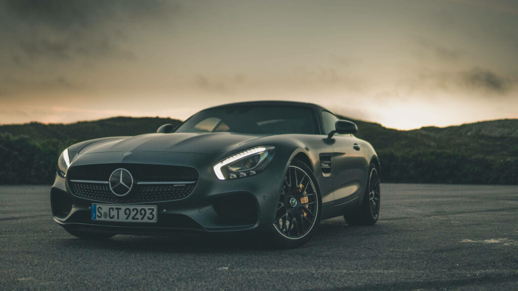 Black Mercedes AMG parked on open road at sunset with dramatic lighting and serene landscape Wallpaper