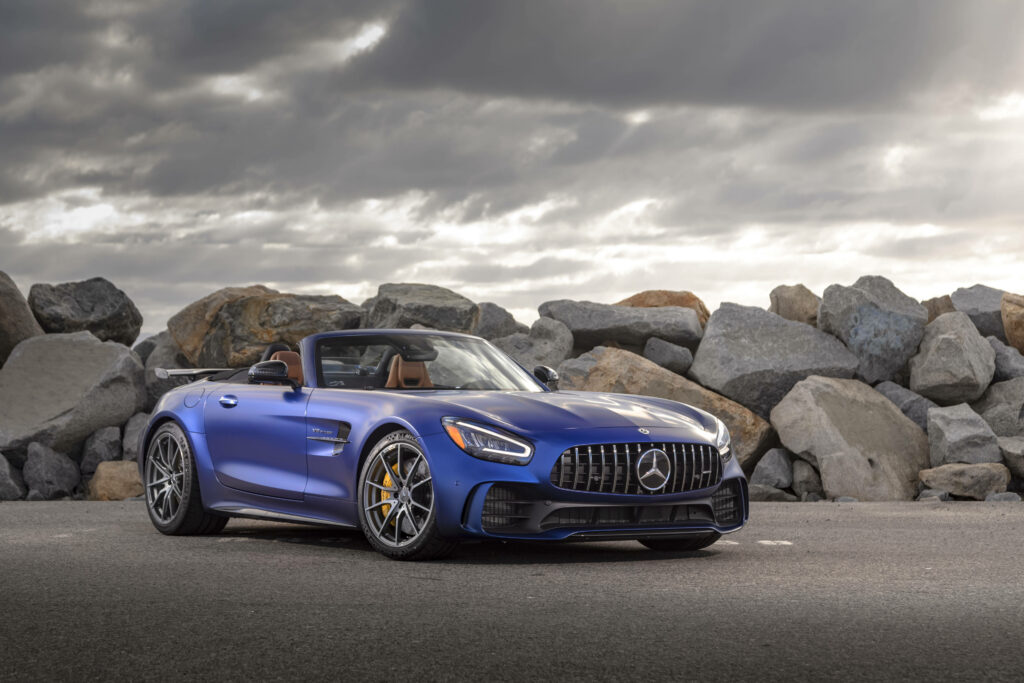 Mercedes AMG GT R vibrant blue sports car parked by rugged rocks under dramatic cloudy sky wallpaper
