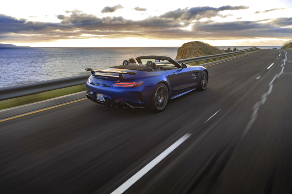 Mercedes AMG GT R driving on coastal road at sunset vibrant skies ocean view wallpaper background