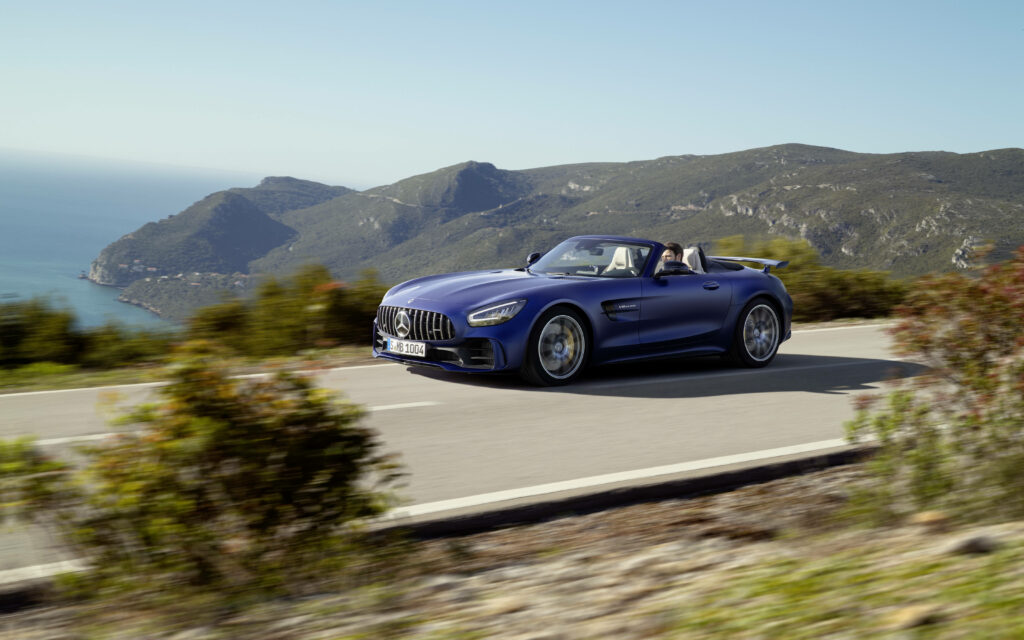 Mercedes AMG GT R speeding on winding hill road with mountains and blue ocean background wallpaper