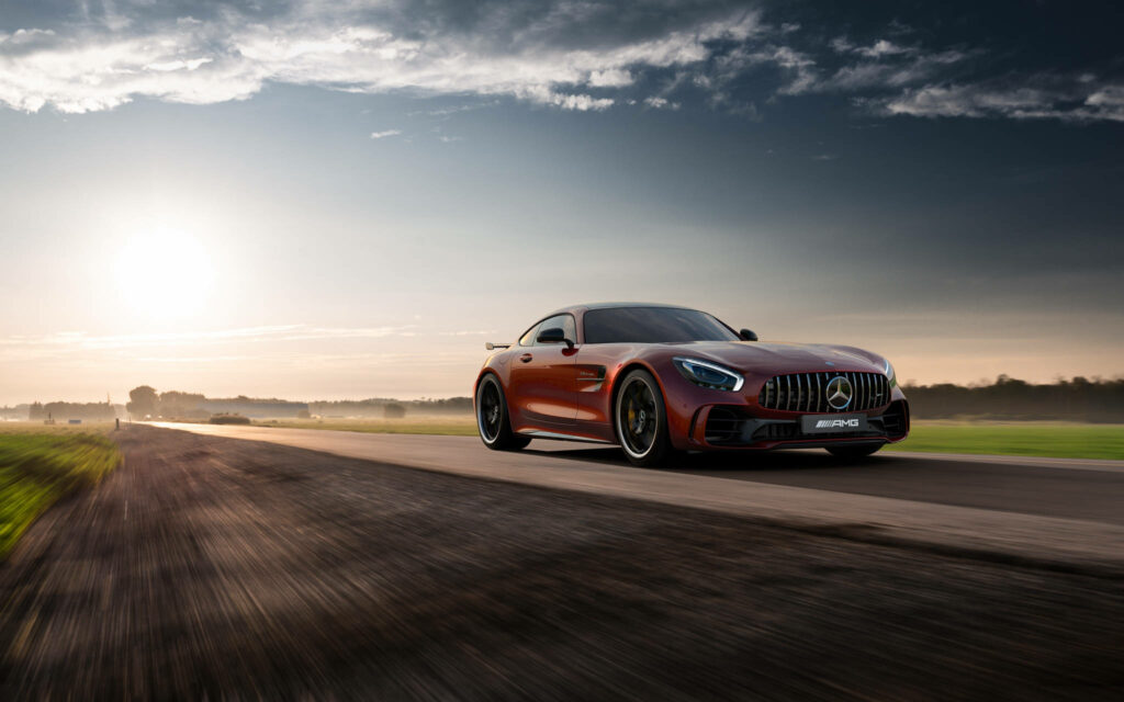 Mercedes AMG GT R speeding on open road at sunrise showcasing sleek design and power Wallpaper