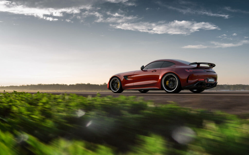 Mercedes AMG GT R speeding on grass road under dramatic sky showcasing bold design and power Wallpaper