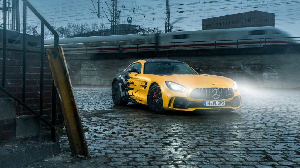 Yellow black Mercedes AMG GT R with LED headlights on wet cobblestone road urban backdrop Wallpaper