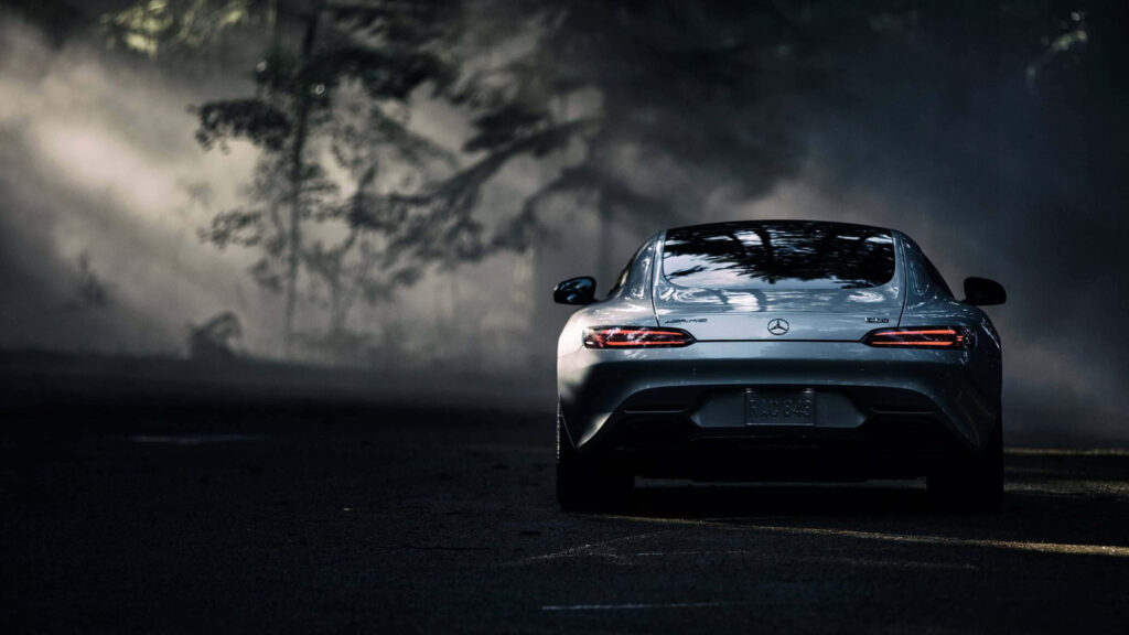 Mercedes AMG rear view in misty forest with light beams highlighting sporty sleek curves wallpaper