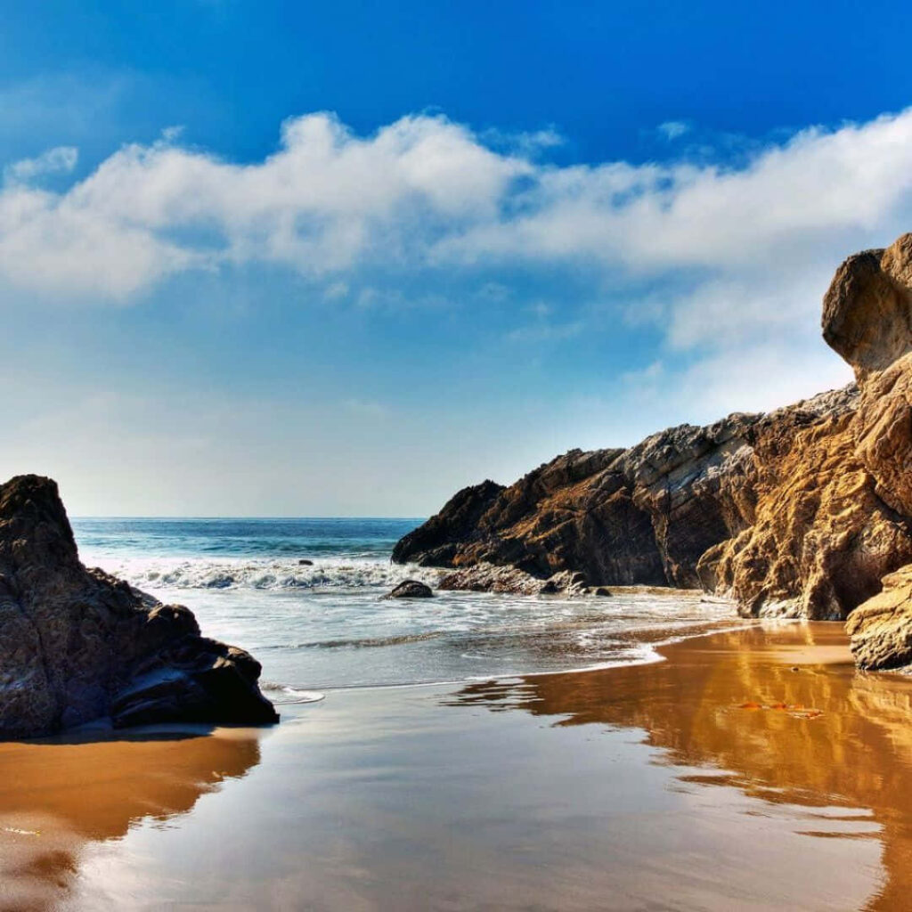 Serene Seascape: Crystal-clear Waters and Majestic Rocks at Malibu Shore Wallpaper