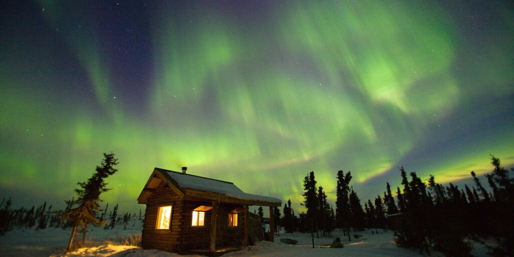Mesmerizing Aurora Borealis Wallpaper: Snowy Cabin Night Scene