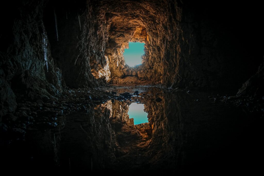 Mesmerizing cave interior with rugged stone walls and clear water reflecting vibrant blue sky Wallpaper