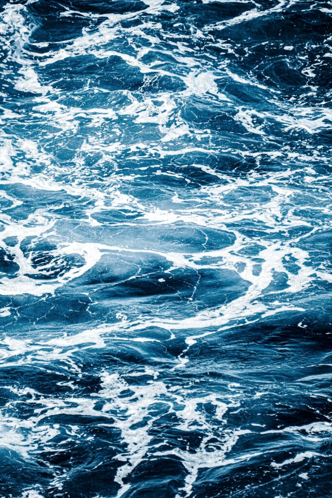 Dynamic ocean waves with white foam in deep blue tones textured wallpaper background