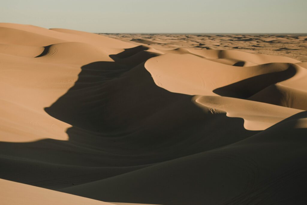 Desert landscape wallpaper with sweeping sand dunes and warm earthy tones in dramatic light