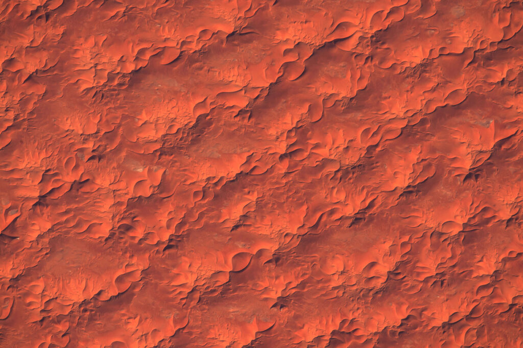 Aerial view of desert sand dunes and textured landforms creating abstract natural patterns Wallpaper