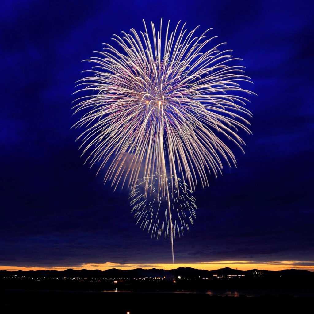Colorful fireworks explode in deep blue night sky over calm landscape festive wallpaper background
