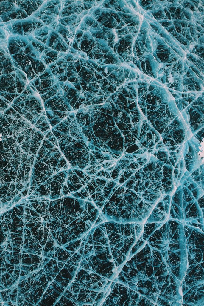 High-angle view of frozen lake with intricate white cracks in deep blue ice abstract pattern Wallpaper
