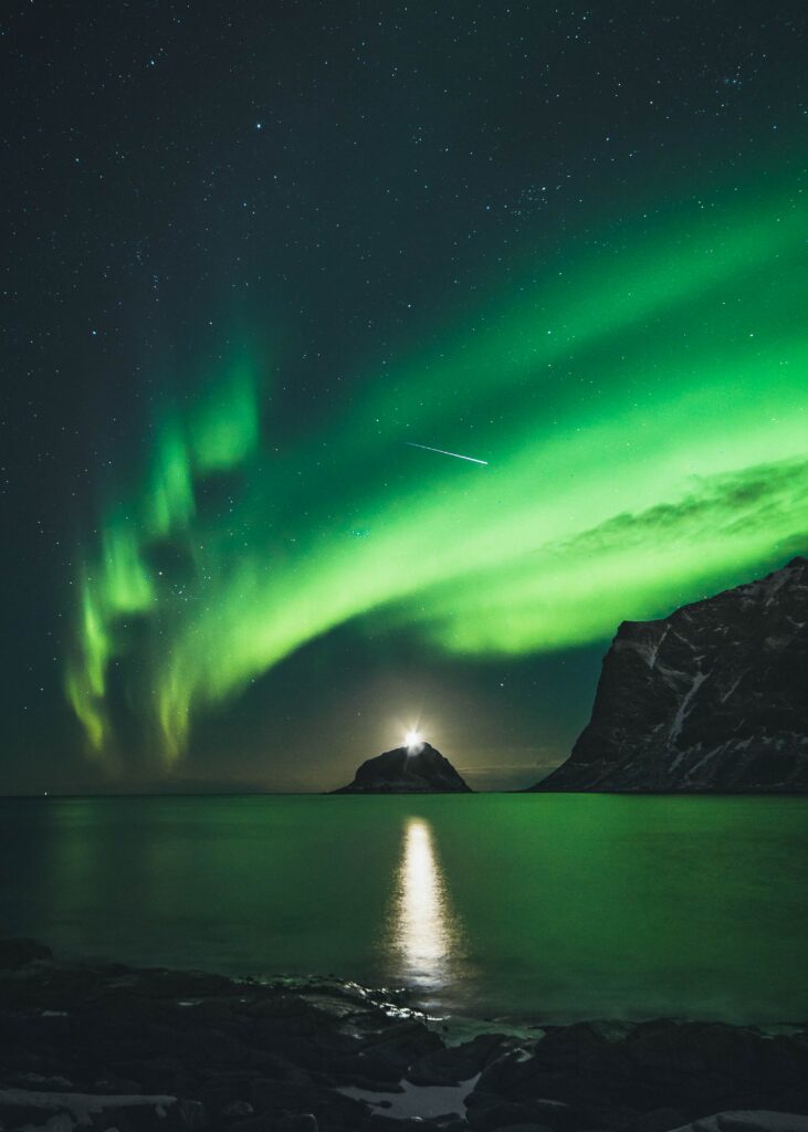 Vivid green northern lights over calm lake with mountains and island reflecting aurora glow Wallpaper
