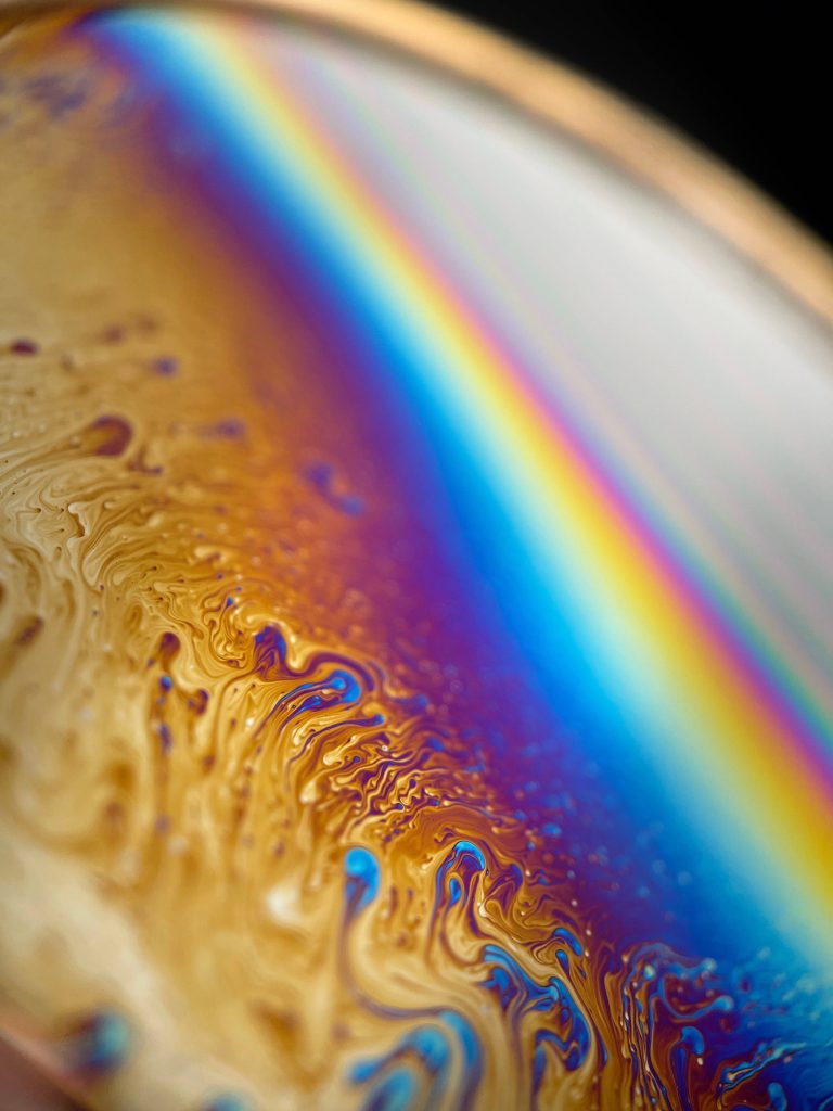 Macro close-up of iridescent soap bubble with swirling golden fluid patterns and rainbow colors Wallpaper