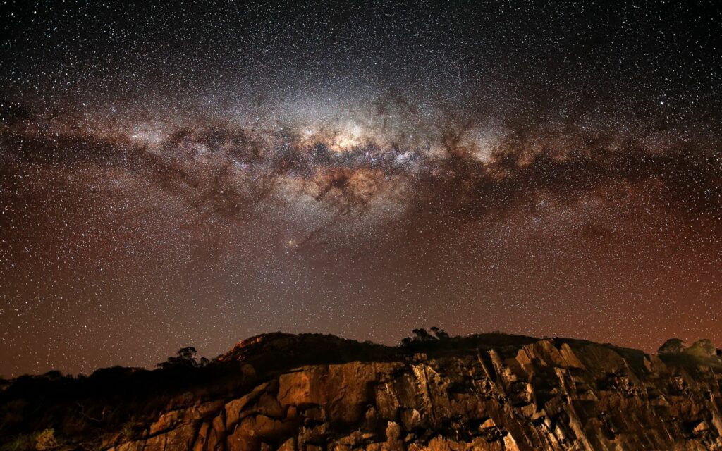 Stunning night sky with Milky Way over rugged mountain rocks in deep earthy tones wallpaper